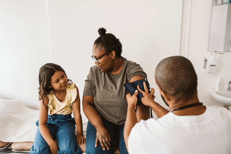 Mother talking with daughter while male doctor measuring blood pressure - stock photo